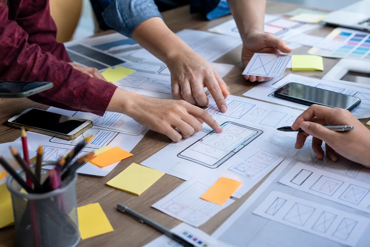 Réunion de travail autour d&rsquo;une table avec smartphones et maquettes d&rsquo;interfaces mobiles